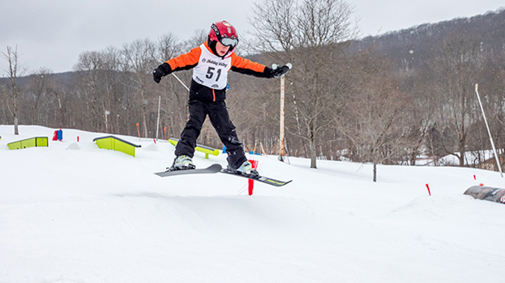 A young skier goes over a small jump in the terrain park